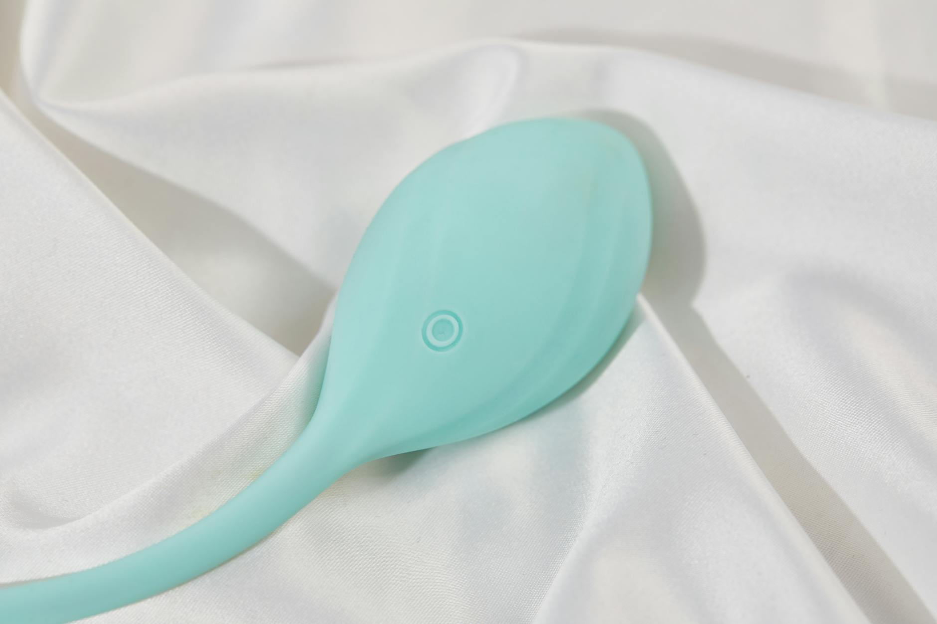 A sleek teal lemon vibrator resting on soft white silk, representing accessible pleasure for mature first-time users.