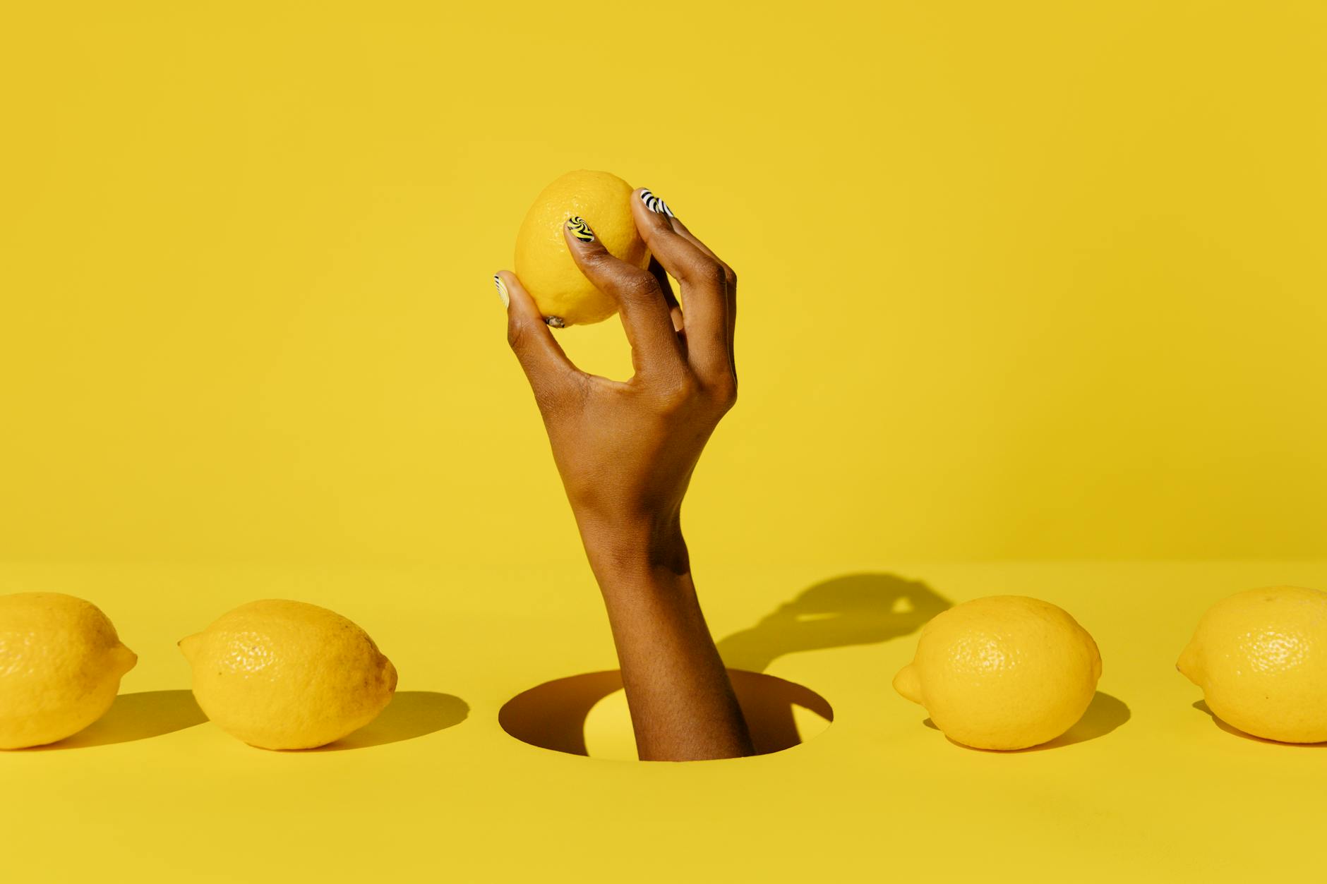 A hand holding a fresh lemon against a vivid yellow background, symbolizing the citrusy design of lemon clitoral vibrators