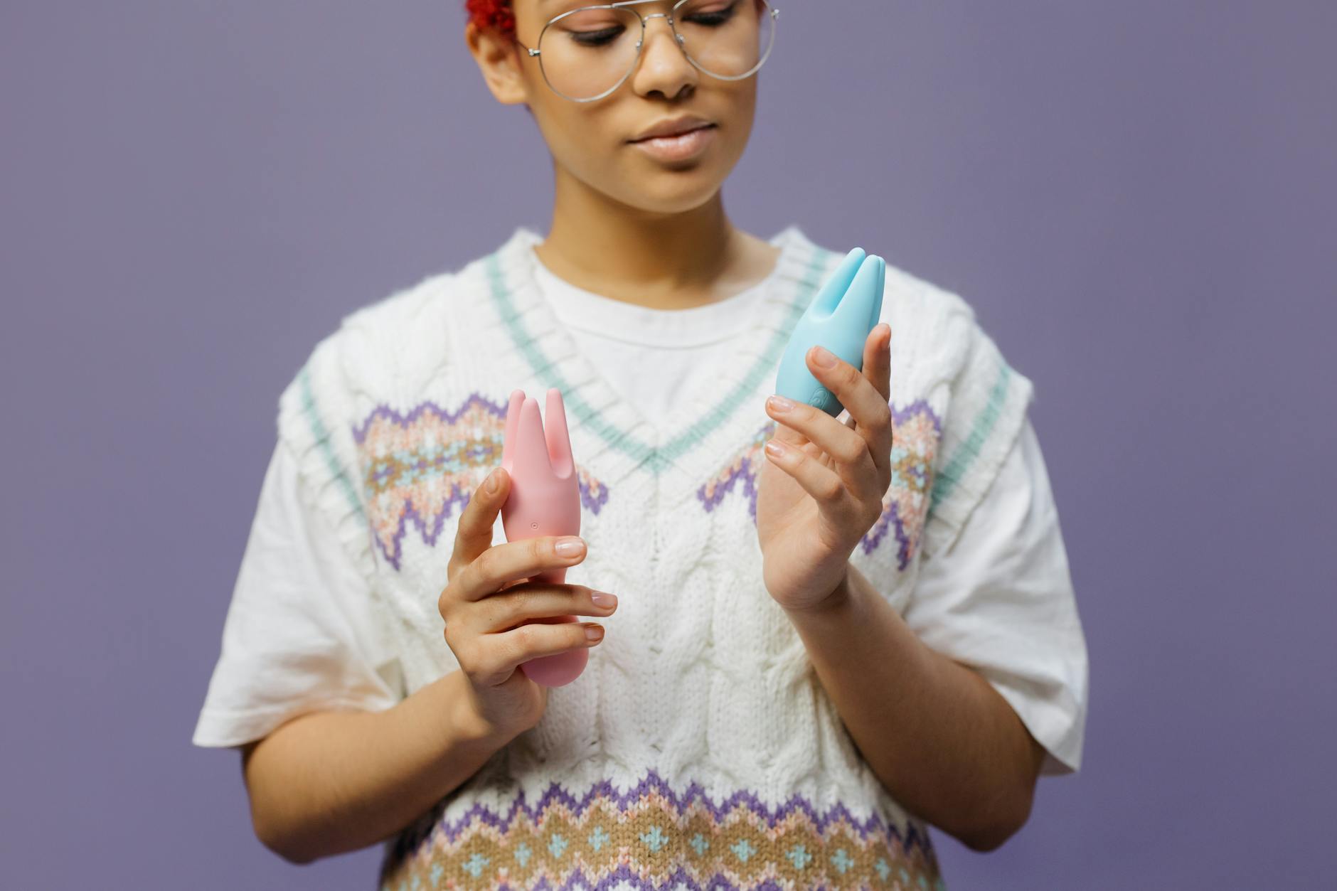 Woman holding blue and pink vibrators thoughtfully, exploring sensation changes