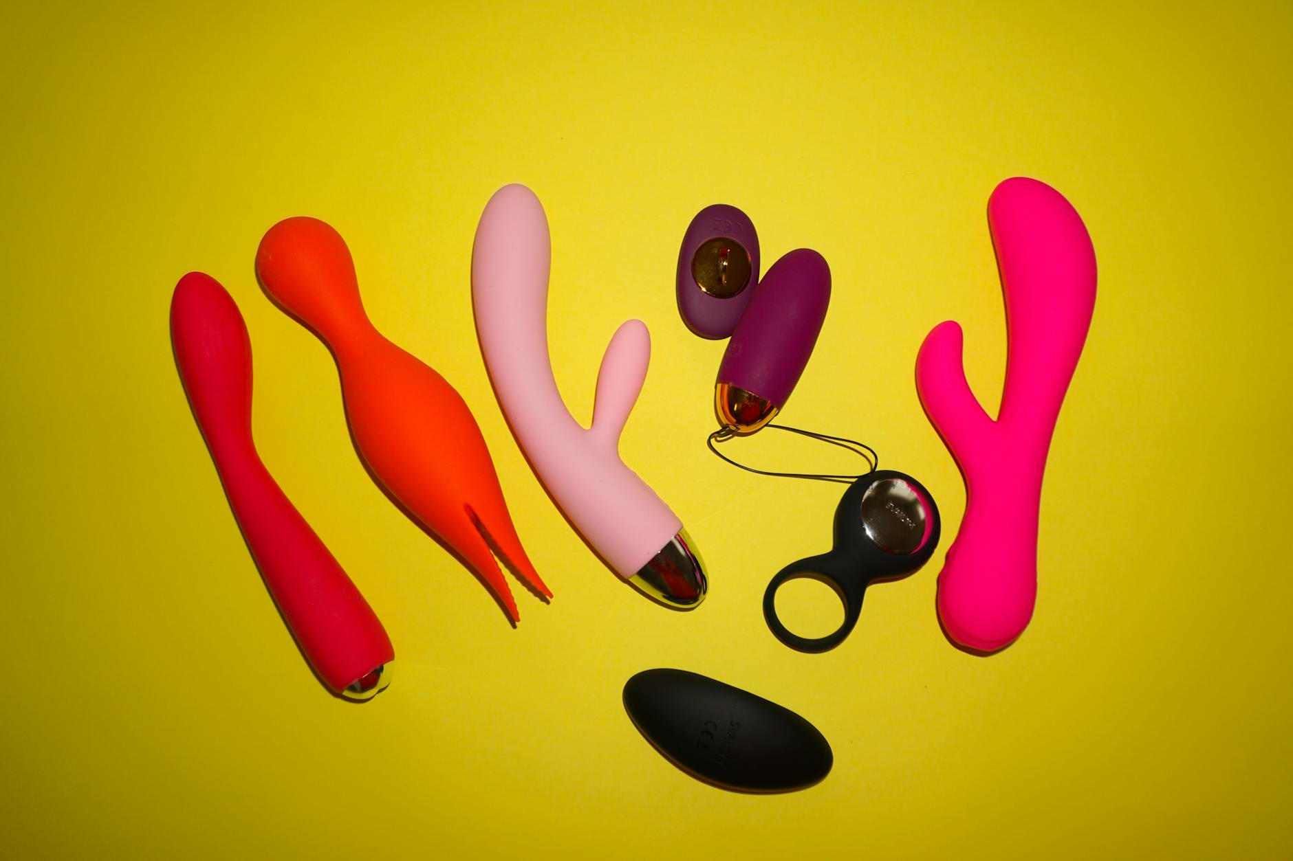 Colorful vibrators and intimate wellness toys arranged on bright yellow background